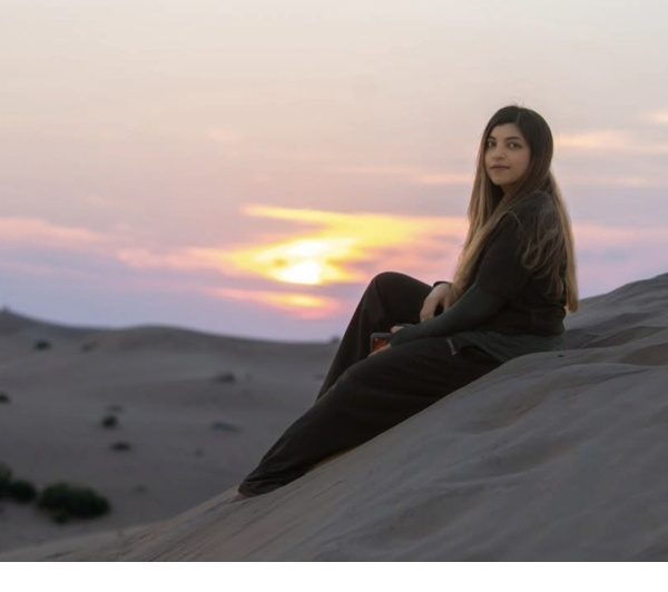 Young woman sitting on a desert dune at golden-hour sunset in the UAE