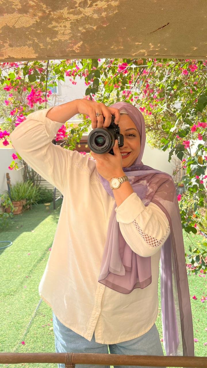 Portrait of Madeeha, founder and photographer at Photos by Madeeha, holding her camera in a sunlit UAE garden